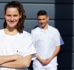 1 jeune femme souriante en blouse blanche, derrière elle un jeune homme en blouse blanche également,